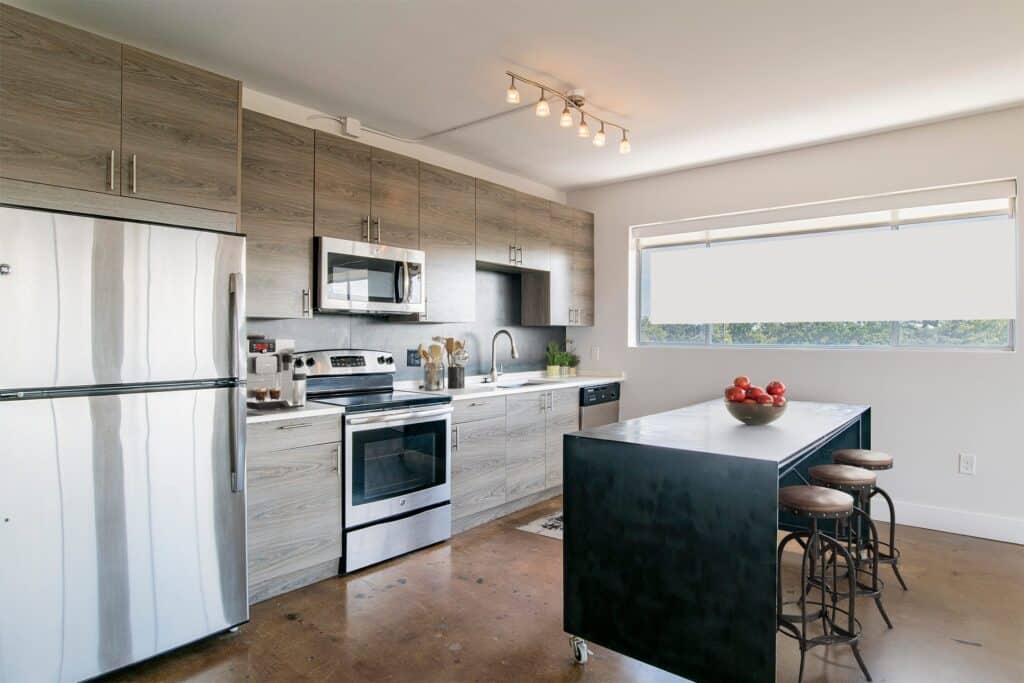 Modern kitchen with stainless steel appliances, wood cabinets, a black island with four stools, and a large window letting in natural light.